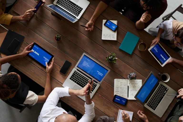 People sat around a meeting table in the workplace using electronic devices